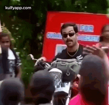 a man is riding a motorcycle and talking to a crowd of people .