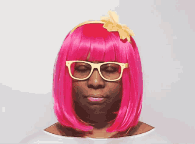 a woman wearing a pink wig and glasses looks at the camera