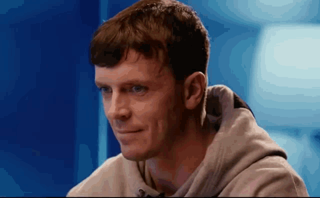 a man in a hoodie is sitting in front of a blue wall .