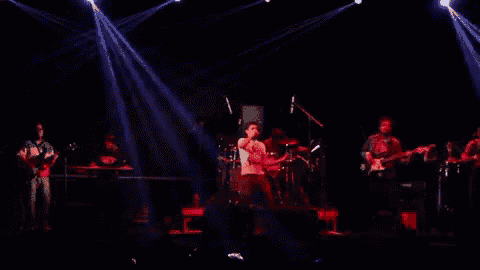 a group of people playing instruments on a stage with red lights behind them