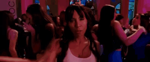 a woman in a white tank top is standing in a crowd of people dancing .