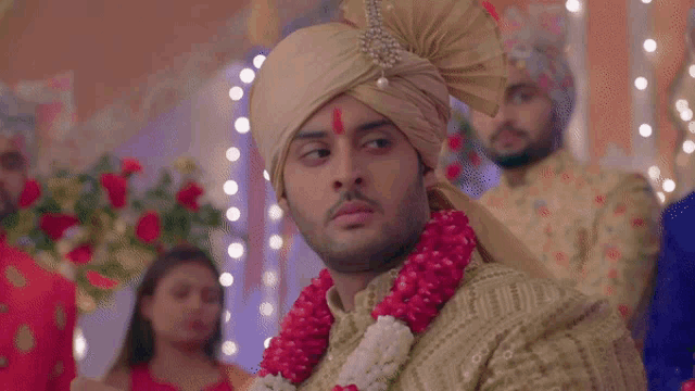 a man wearing a turban and a garland of flowers looks at the camera