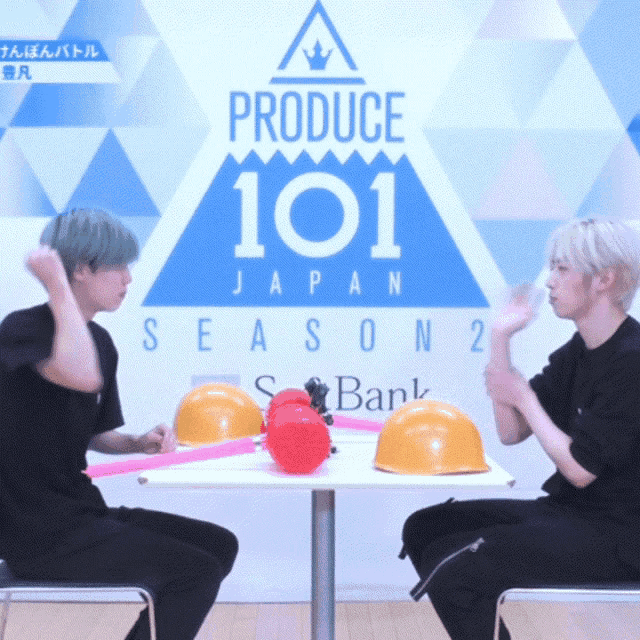 two men sitting at a table in front of a sign that says produce 101 japan