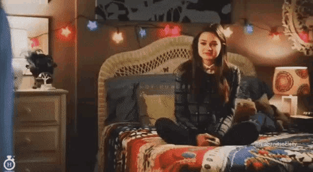 a girl is sitting on a bed in a bedroom with christmas lights .