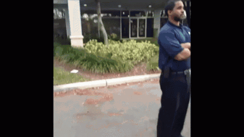 a man in a blue shirt and black pants is standing in front of a building with his arms crossed