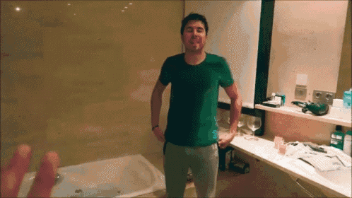 a man in a green shirt stands in front of a bathtub