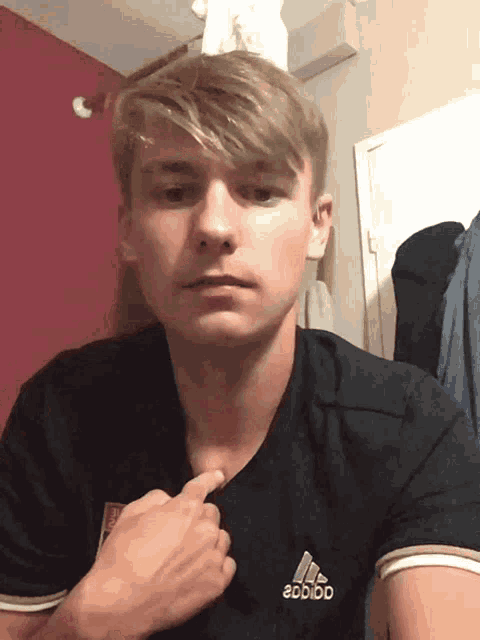 a young man is wearing an adidas shirt and pointing to his chest