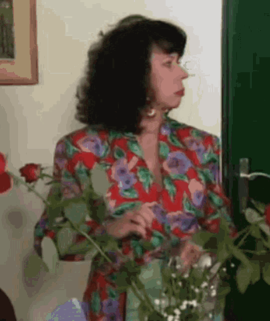 a woman in a colorful floral shirt stands in front of a green door
