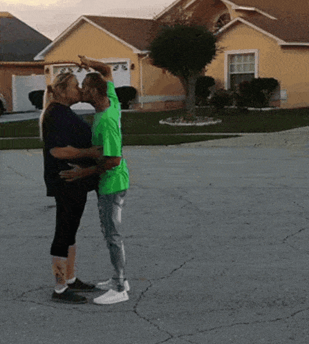 a couple kissing in front of a yellow house