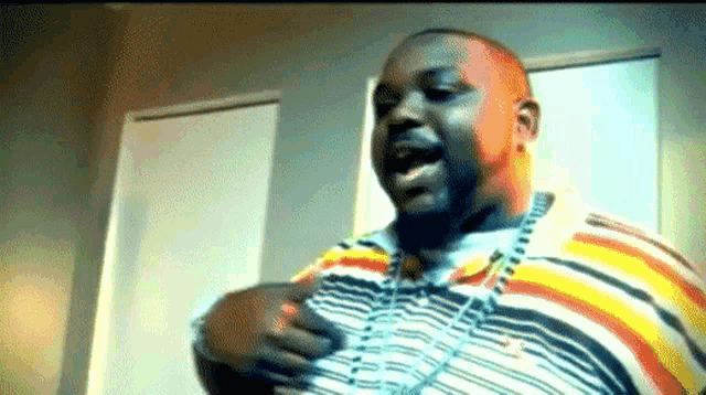 a man wearing a striped shirt and a necklace is singing