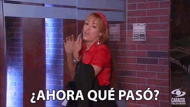 a woman in a red shirt is standing in front of a brick wall and says ahora que pasó