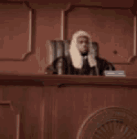 a man in a wig is sitting at a podium in a courtroom .