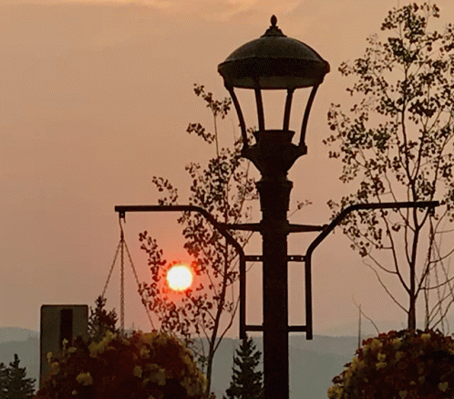 the sun is setting behind a street lamp