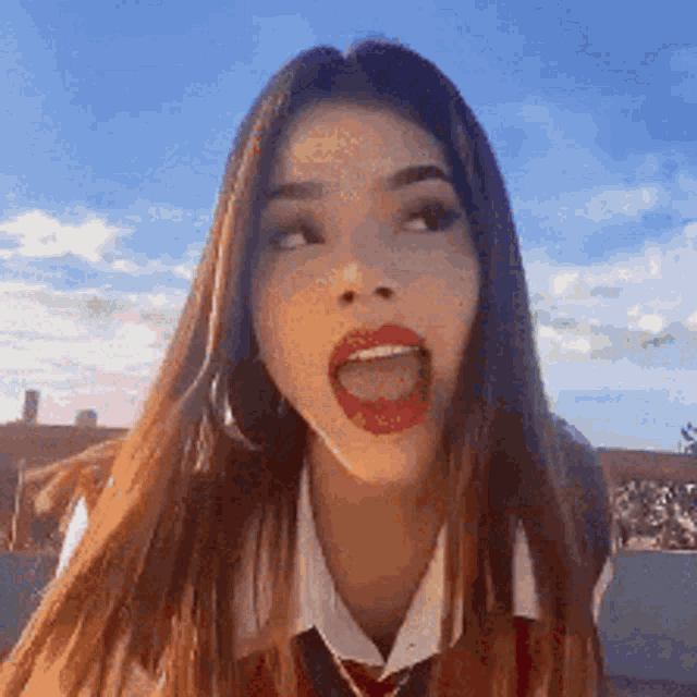 a woman with long hair and red lipstick is sticking out her tongue .