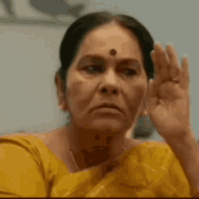 a woman in a yellow shirt is making a funny face with her hand