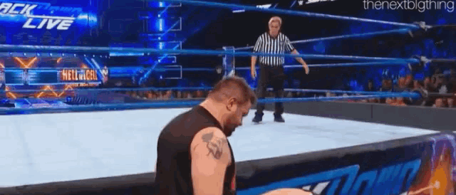 a wrestler is kneeling down in a wrestling ring with a referee in the background