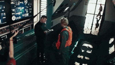 a man in an orange vest is talking to another man in front of a computer screen