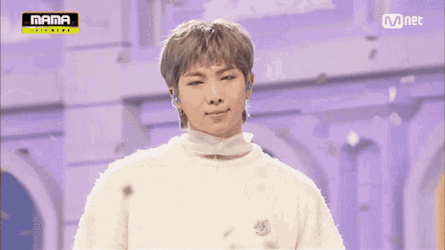 a man wearing a white sweater is smiling in front of a mnet logo