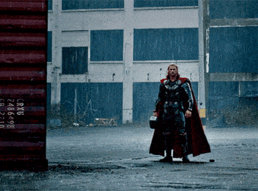 a man in a cape stands in the rain in front of a shipping container that says crxu