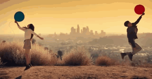 a man and a woman are jumping in the air with balloons in front of a city