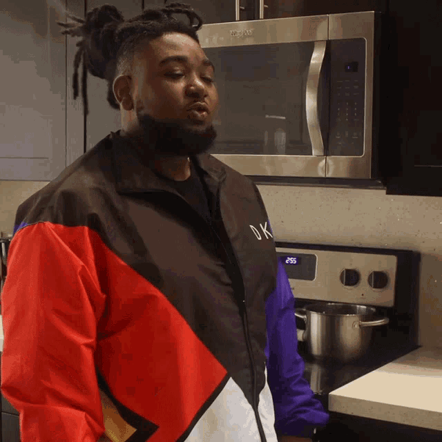 a man wearing a jacket that says dk stands in front of a microwave