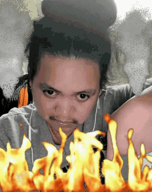 a man with a bun on his head and a bunch of flames behind him
