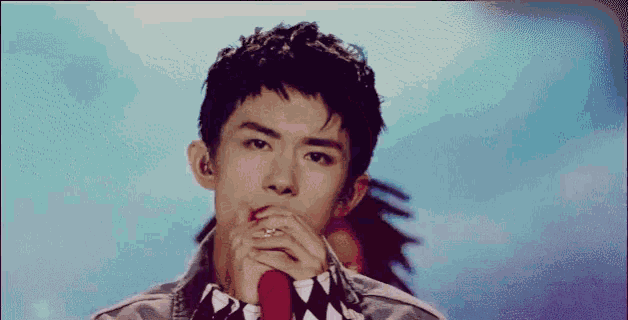 a young man is singing into a microphone with his hands folded