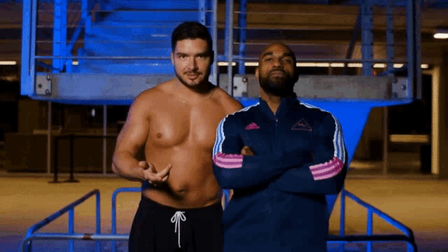 two men standing next to each other with one wearing a blue adidas jacket