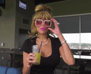 a woman wearing sunglasses holds a drink in front of a sign reading 306