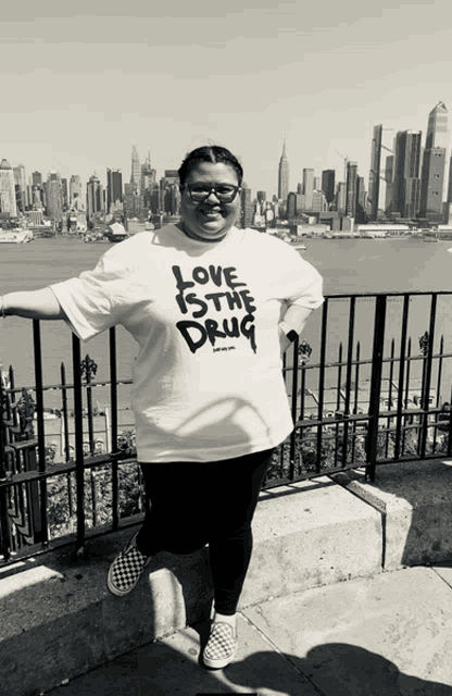 a woman wearing a t-shirt that says love is the drug stands in front of a city skyline