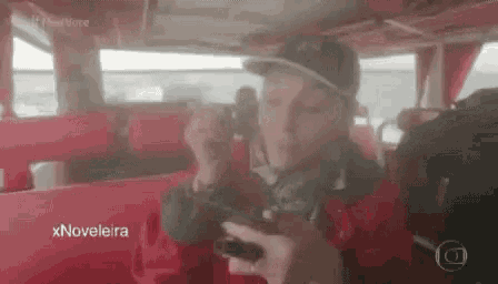 a man is sitting in a red bus holding a camera and a cell phone .