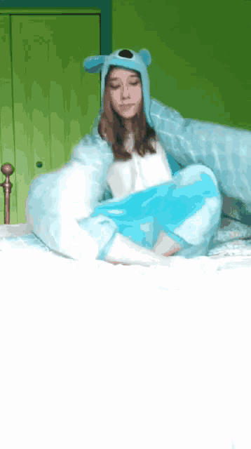 a girl wearing a blue hat and a blue blanket is sitting on a bed