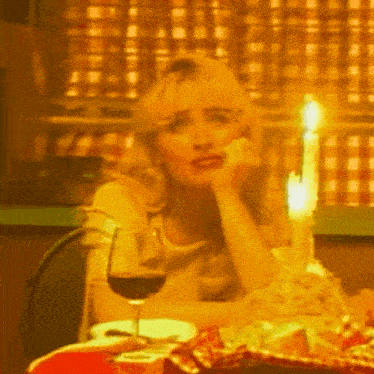 a woman is sitting at a table with a glass of wine and a candle