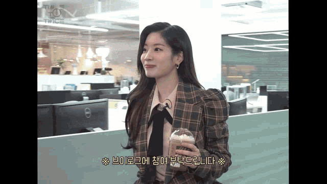 a woman in a plaid jacket is holding a cup of coffee in an office
