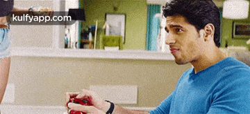 a man in a blue shirt is sitting on a couch holding a red object in his hand .