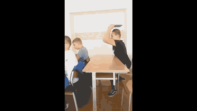 a group of children are sitting at a table in a classroom and one of them is holding another child 's head .
