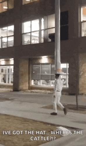 a man walking down a sidewalk with the words " i 've got the hat ... where 's the cattle "