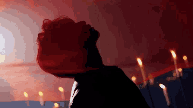 a person with red hair is standing in front of a wall of candles