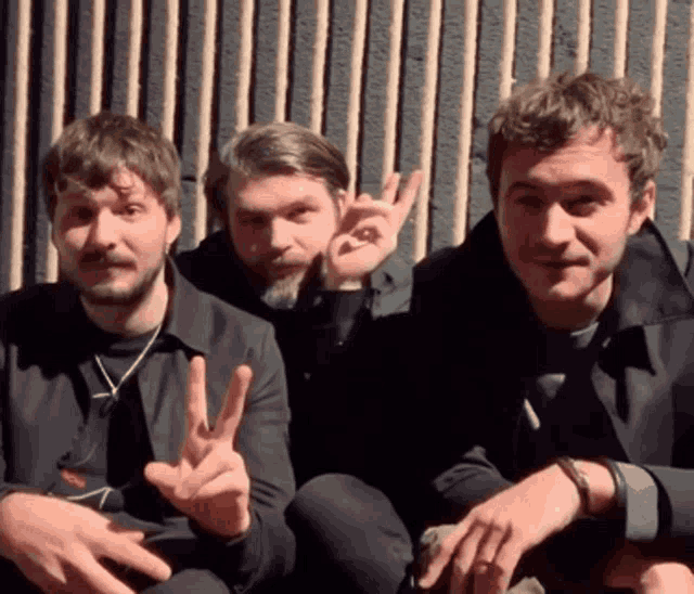 three men are sitting next to each other and one of them is giving a peace sign