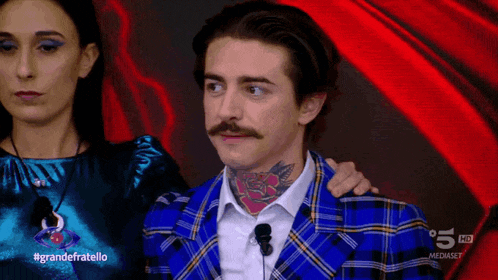 a man with a mustache and a blue plaid jacket stands next to a woman with the hashtag grandefratello