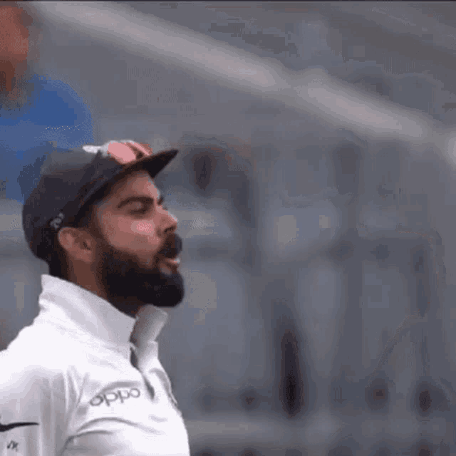a man with a beard and sunglasses is wearing a hat and a white shirt .