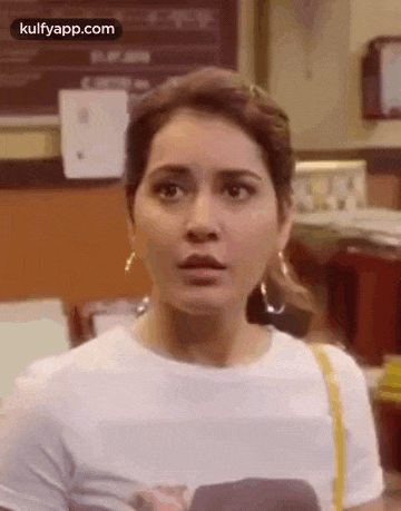 a woman wearing a white t-shirt and earrings is making a surprised face .
