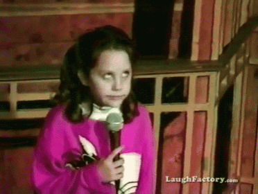 a girl in a pink sweater is holding a microphone in front of a sign that says laugh factory