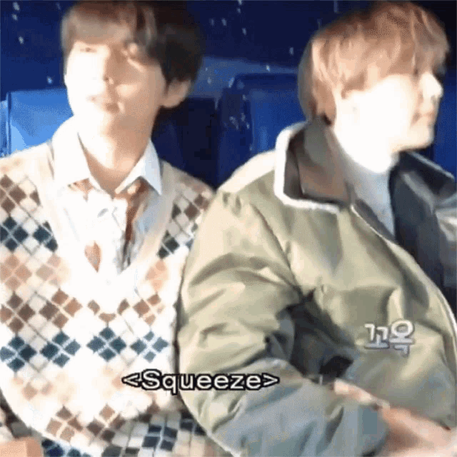 two young men are sitting next to each other and one of them is squeezing the other