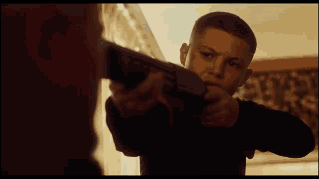 a young boy is holding a shotgun in front of a man
