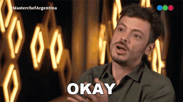 a man in a green shirt says " okay " in front of a neon sign