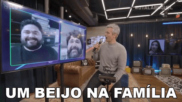 a man is holding a microphone in front of a large screen that says um beijo na familia on it