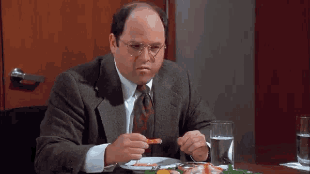 a man is sitting at a table with a plate of food and a glass of water and the name jason alexander is on the bottom
