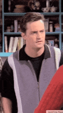 a man in a black shirt and a blue vest stands in front of a shelf