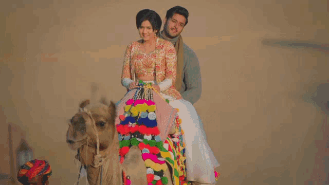a man and a woman ride on the back of a decorated camel
